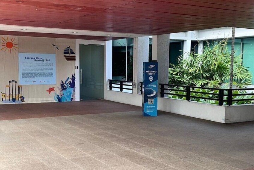 A modern building entrance with a sign for Sentosa Cove, a blue sign for Meeting Point, and a planter with green plants. 4
