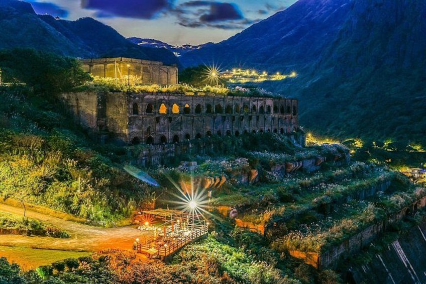 Una estructura de piedra histórica con arcos, rodeada de exuberante vegetación y montañas al fondo. 2