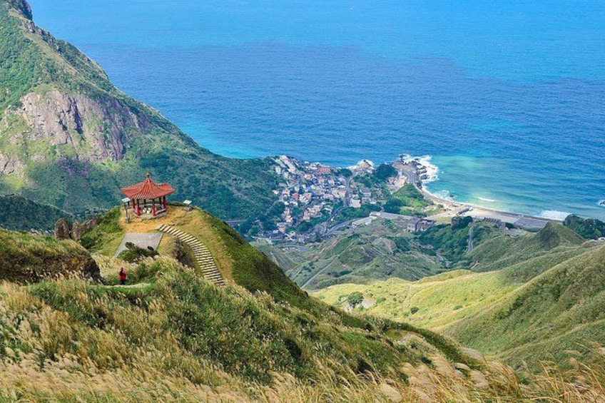 Un paisaje costero con un pabellón rojo en una colina, un camino sinuoso y un pueblo junto al mar. 5