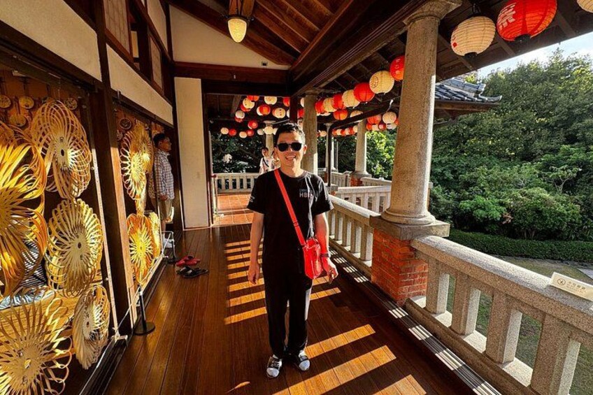 A person standing on a wooden walkway with lanterns overhead and decorative panels on the walls. 4