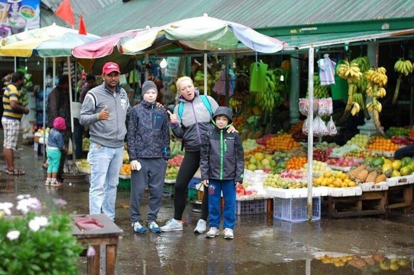Un mercato con persone sotto ombrelli, circondato da bancarelle che vendono frutta e verdura. 1