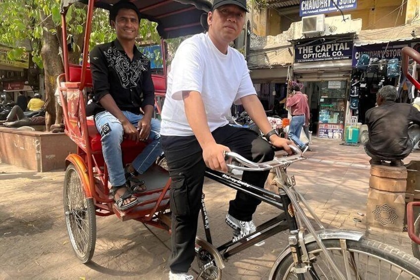 En man som skjuter en cykel framför sig och har en rickshaw efter sig. I bakgrunden syns en butik med namnet ”The Capital Optical Co.”. 4