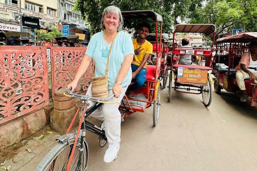 En person som cyklar på en gata med en röd rickshaw i bakgrunden. 5