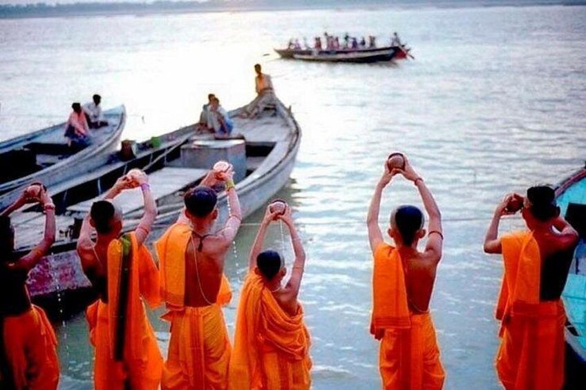 Monks in orange robes performing a ritual by the water. 3