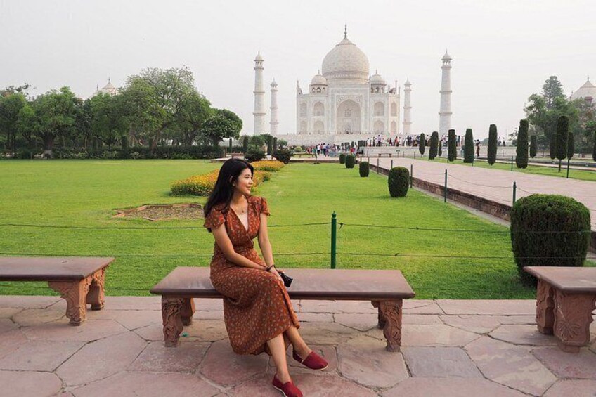 A woman sitting on a bench with the Taj Mahal in the background. 3