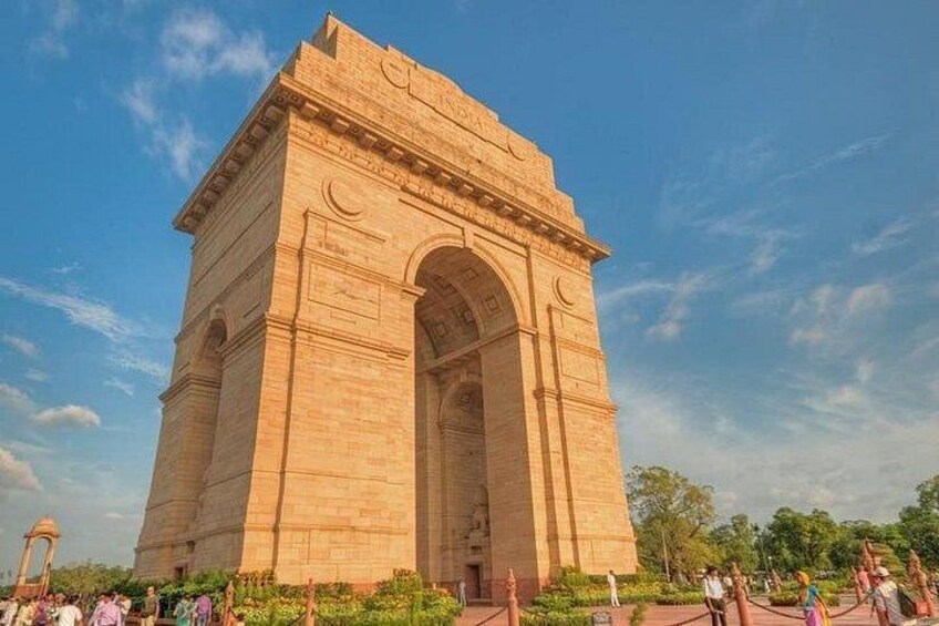 A large stone monument with an archway, surrounded by greenery and people. 5
