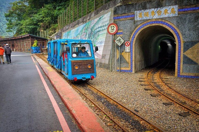 A blue train at a station with a tunnel entrance, a speed limit sign, and a no smoking sign. 5