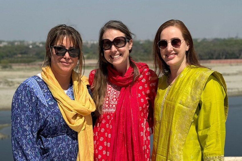 Tres personas de pie junto a un cuerpo de agua, con cielo despejado al fondo. 3