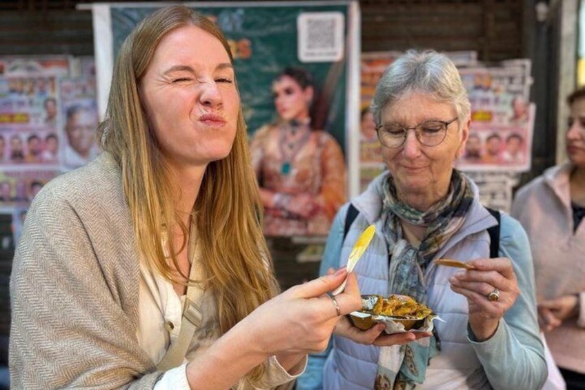 Two people eating at a street food stall with a poster in the background. 5
