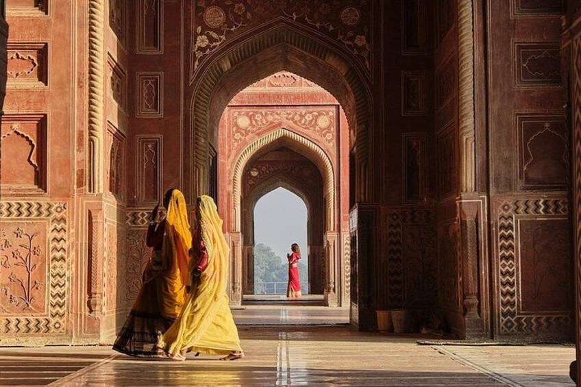 An ornate archway with intricate designs, a person in a red dress standing at the end, and two individuals in traditional attire. 2