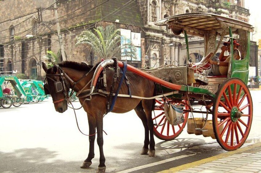 A horse-drawn carriage with red wheels and ornate decorations, parked on a street with a historic building in the background. 1