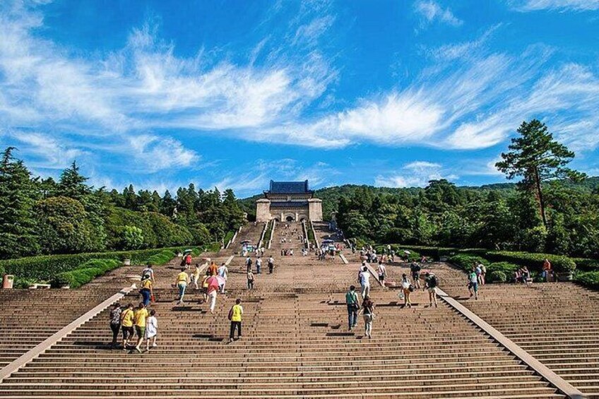 A large open plaza with steps leading to a traditional building, surrounded by trees and greenery. 2