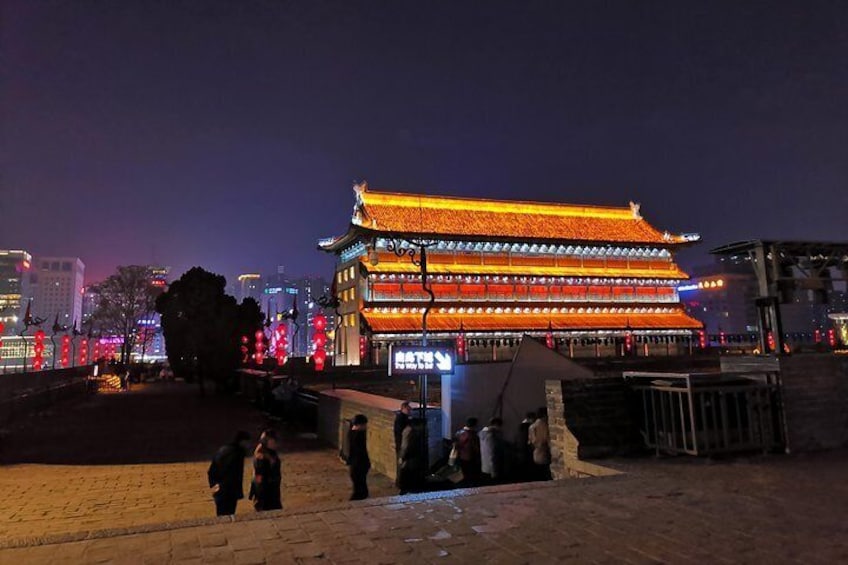 A traditional building with illuminated red and yellow lights, surrounded by a paved area with people walking. 2
