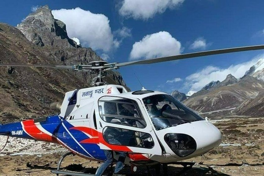 Ein Hubschrauber mit roter, weißer und blauer Bemalung steht auf felsigem Gelände, im Hintergrund sind Berge zu sehen. 5