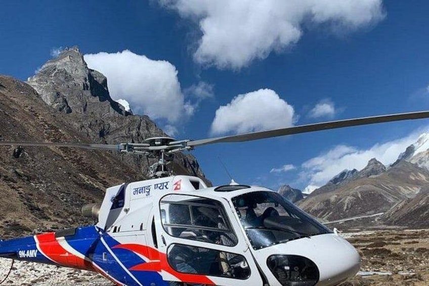Ein Hubschrauber mit rotem, weißem und blauem Heckflossen, geparkt auf felsigem Gelände vor einer Bergkulisse. 2