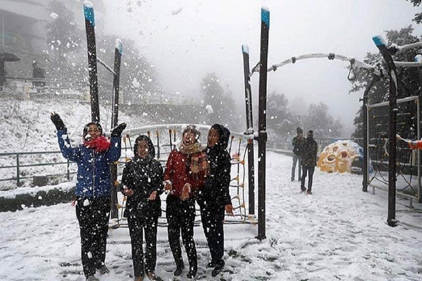 A group of people standing in a snowy park with a playground structure in the background. 3