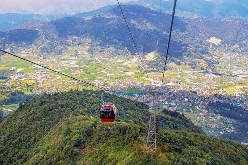 A cable car suspended over a mountainous landscape with a town below. 1