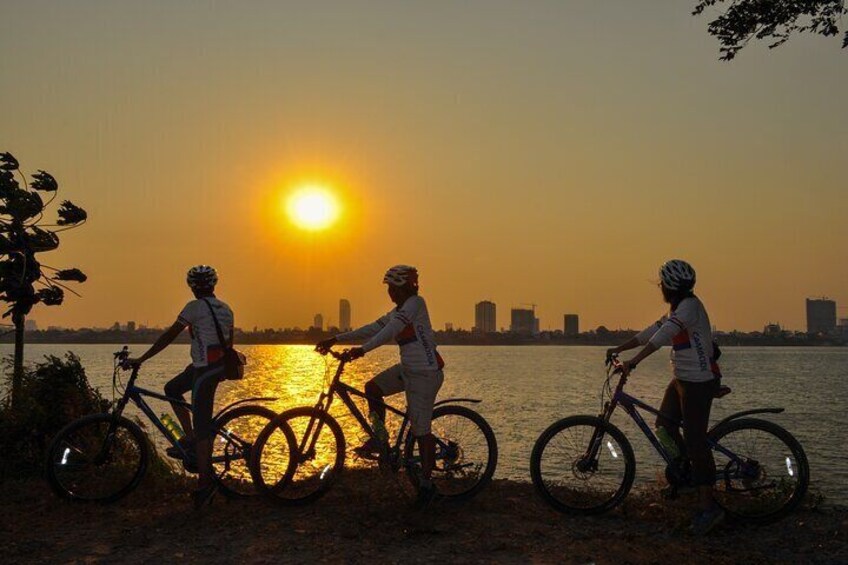 Tres ciclistas en un sendero junto al agua al atardecer. 1