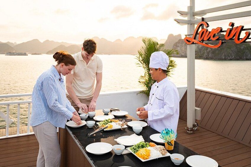 A dining area on a boat with a chef preparing food, a person serving, and a scenic view of the water and mountains in the background. 5