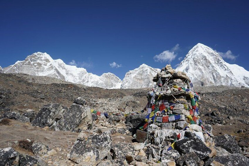A snow-covered mountain range with a prayer flag cairn in the foreground. 2