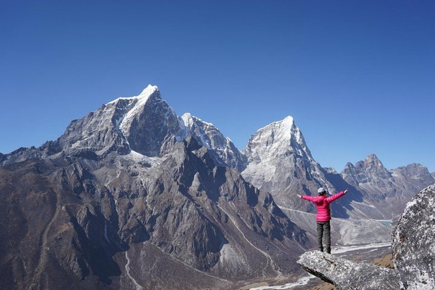A person standing on a rocky outcrop with arms outstretched, overlooking a mountain range with snow-capped peaks. 3