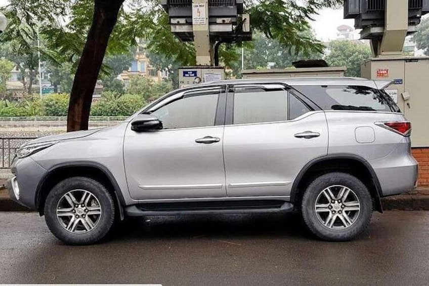 A silver SUV parked on a wet road with trees and buildings in the background. 3