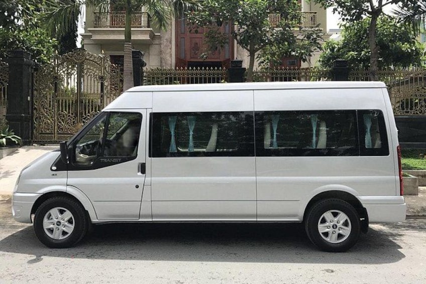 A white van parked on a street with a gated entrance and trees in the background. 2