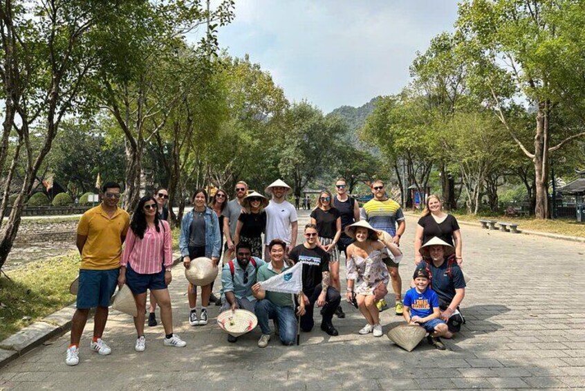 A group of people posing for a photo in a park with trees and a paved path. 2