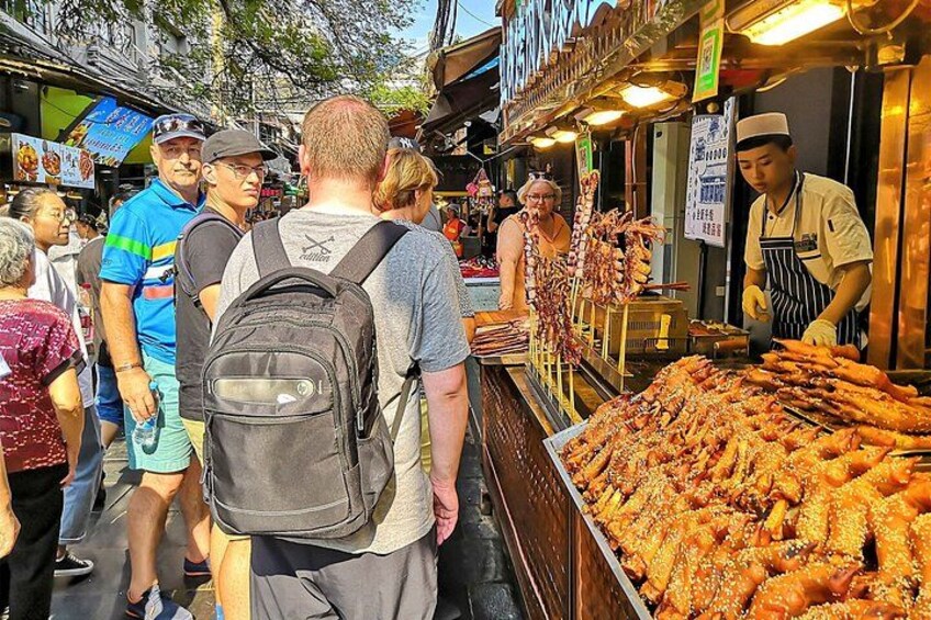 A street food market with people standing in line and a vendor preparing food. 2