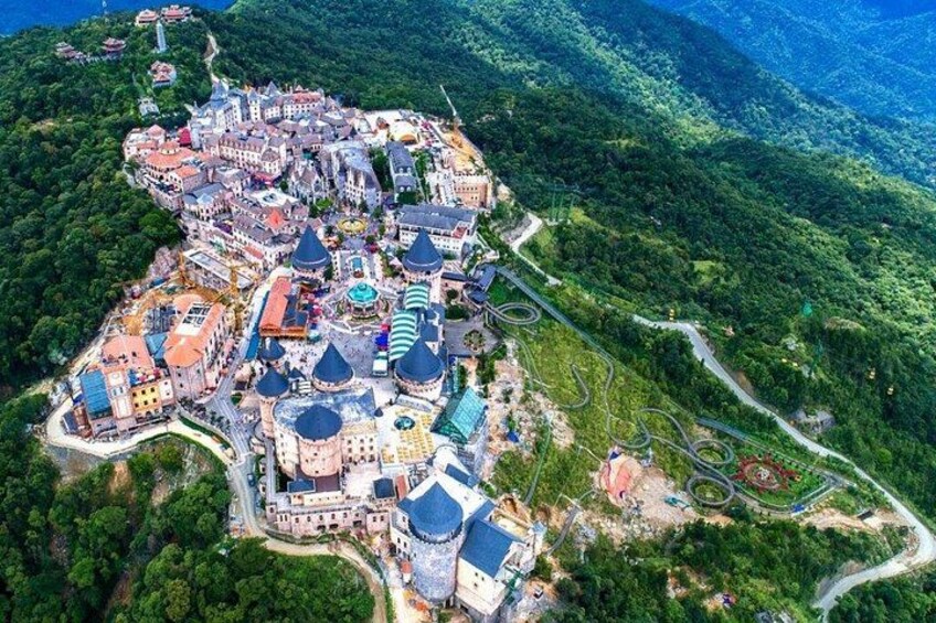 Vista aérea de un pueblo histórico con un castillo, carreteras sinuosas y abundante vegetación. 5