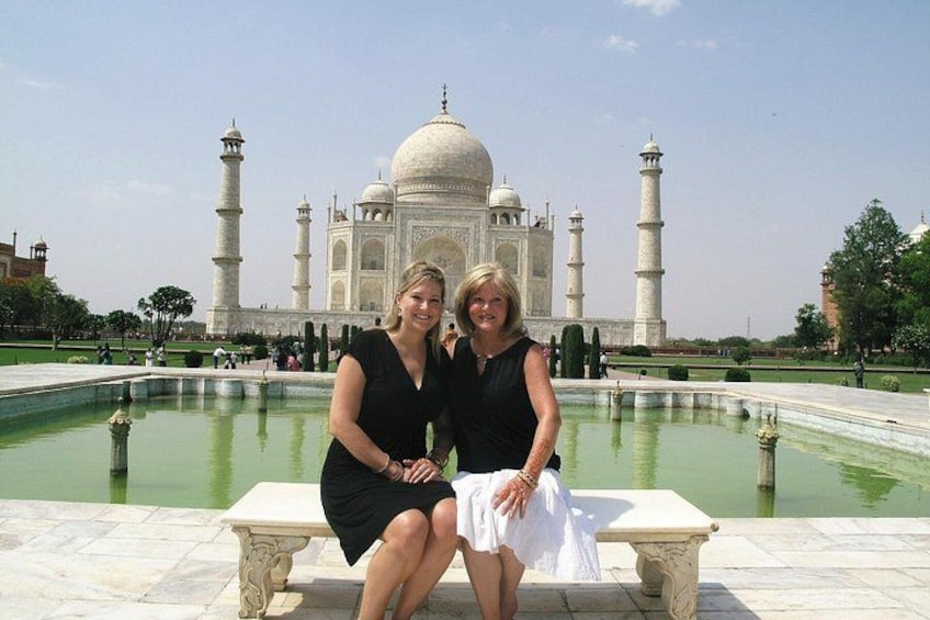 Two people sitting on a bench in front of the Taj Mahal. 1