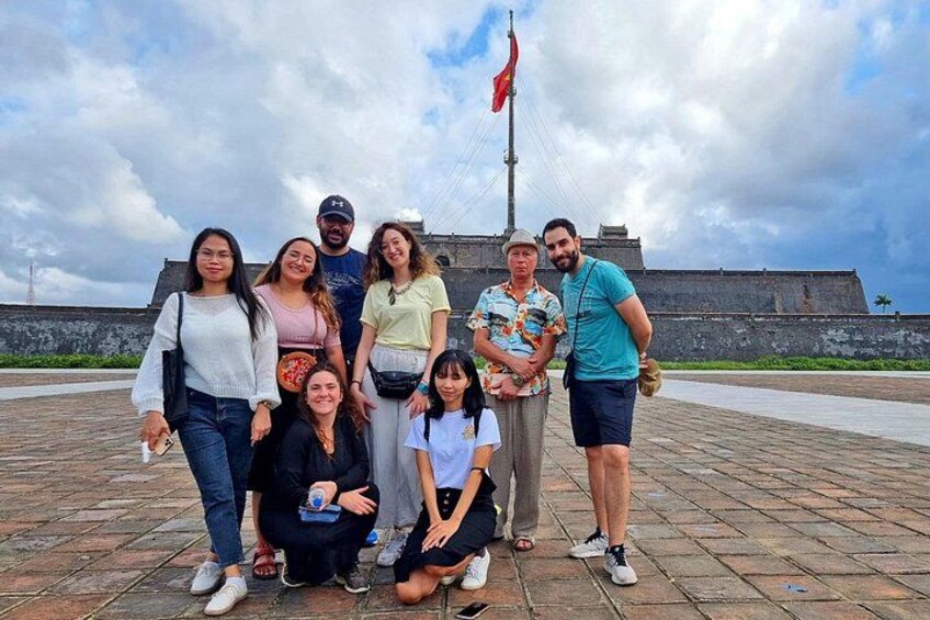 A group of people posing in front of a historical fort with a flag. 3