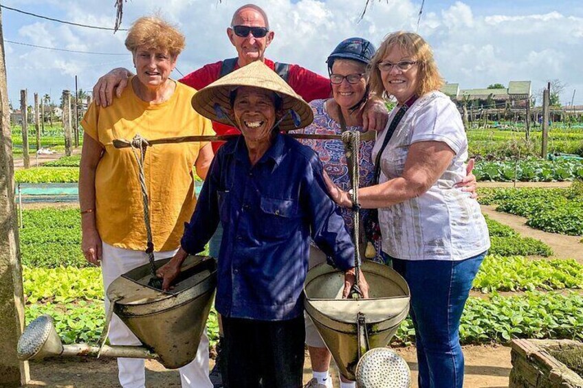 A group of people standing in a field with green crops, holding farming tools. 3