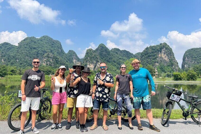 A group of people standing by a lake with bicycles, surrounded by green hills. 1