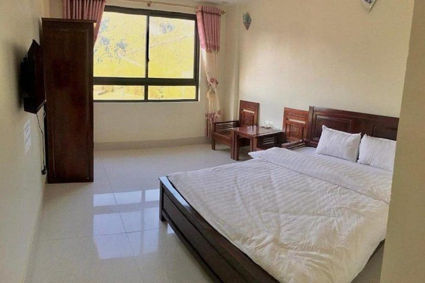 A bedroom with a large bed, a wooden wardrobe, a desk, and a window with curtains. 2