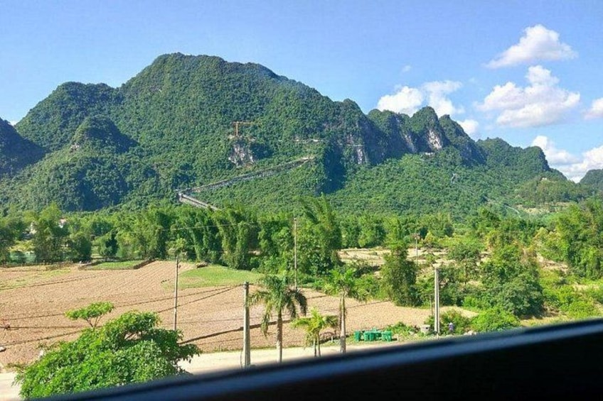 A mountainous landscape with lush greenery, a clear sky, and a road with a bridge. 3