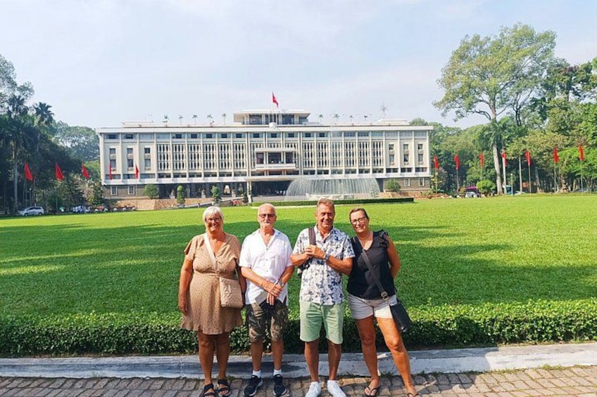 Eine Gruppe von Menschen steht vor einem großen Gebäude mit einer Flagge auf dem Dach, umgeben von einem gepflegten Rasen und Bäumen. 3