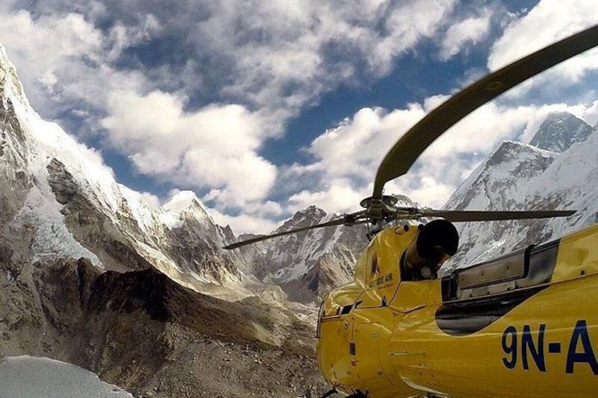 En gul helikopter med registreringsnummer 9N-A i et bjergrigt område med sneklædte tinder. 1