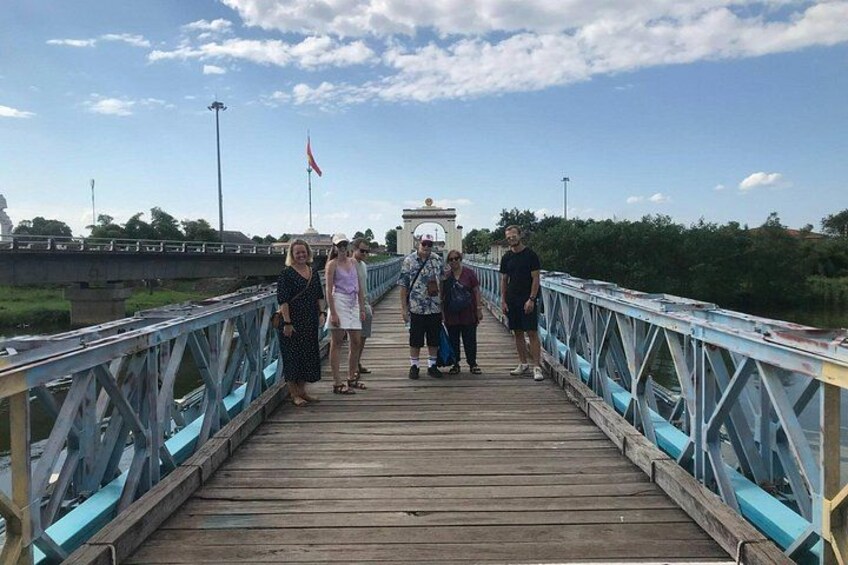 Un puente peatonal de madera con barandillas de metal, una bandera y un monumento distante. 5