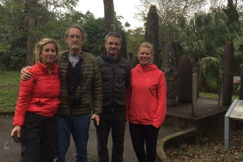 Quatre personnes se tiennent debout dans un parc, devant des structures en pierre et au milieu de la verdure. 2