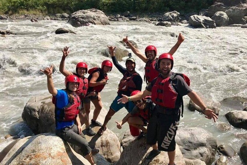 A group of people wearing life jackets and helmets, standing on rocks by a flowing river. 5