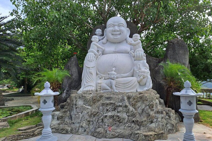 Una gran estatua blanca de una figura sentada con múltiples brazos, rodeada de rocas y follaje. 2