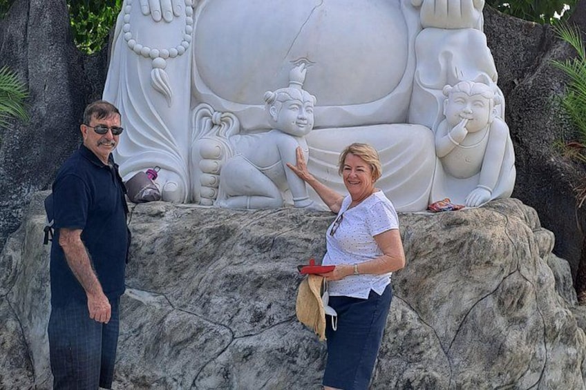 Dos personas de pie frente a una gran escultura blanca con varias figuras. 3