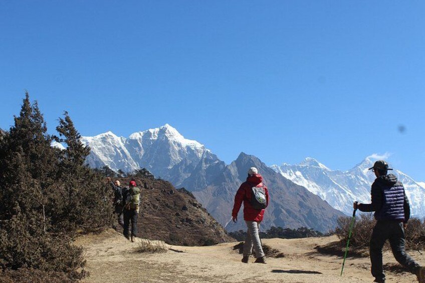 Three hikers on a dirt path with snow-capped mountains in the background. 1