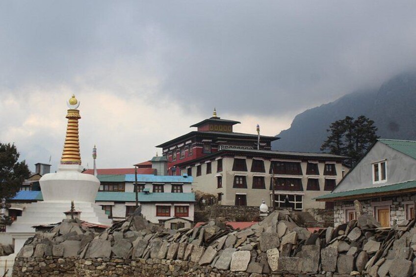 A white stupa with a golden top, a multi-story building with a red and blue roof, and a mountainous backdrop. 5