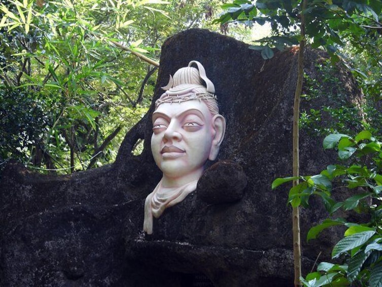 En stenhugget statue af en figur med hovedbeklædning, omgivet af frodig vegetation. 2