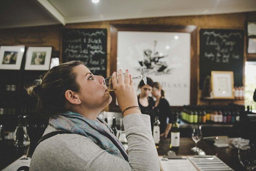 A person drinking from a glass at a bar with a chalkboard menu in the background. 2