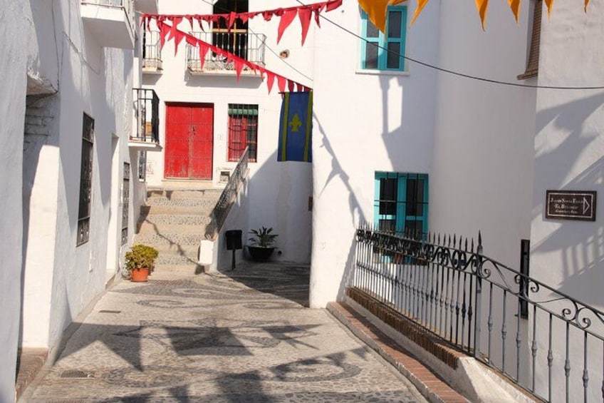 Une rue étroite bordée de bâtiments blancs, de portes rouges et d’une clôture en fer forgé noir. 2