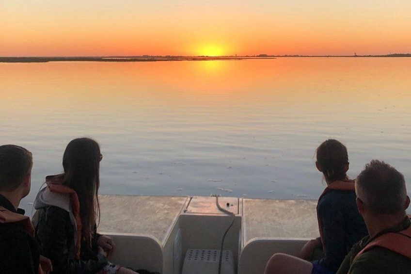 A sunset over a calm body of water with a group of people on a boat. 3