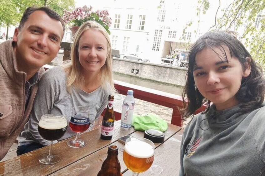 Drie personen zitten aan een houten tafel buiten, met drankjes en een biertje. 4